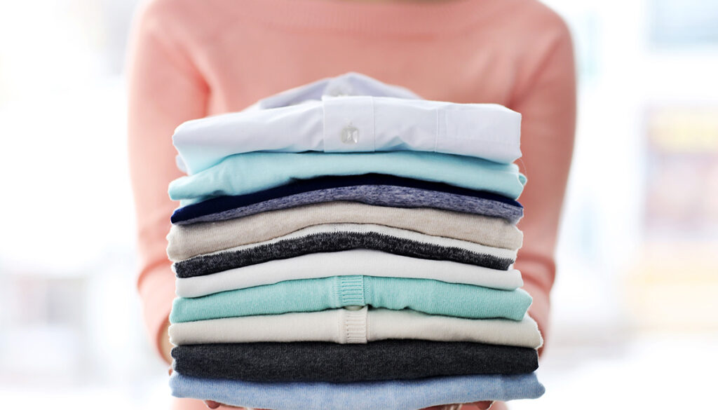 woman-holds-stack-of-colorful-folded-clothing